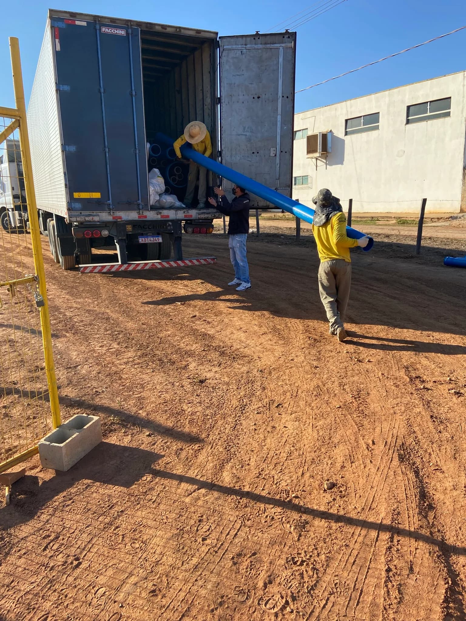 Trabalhadores descarregando tubos azuis de PVC