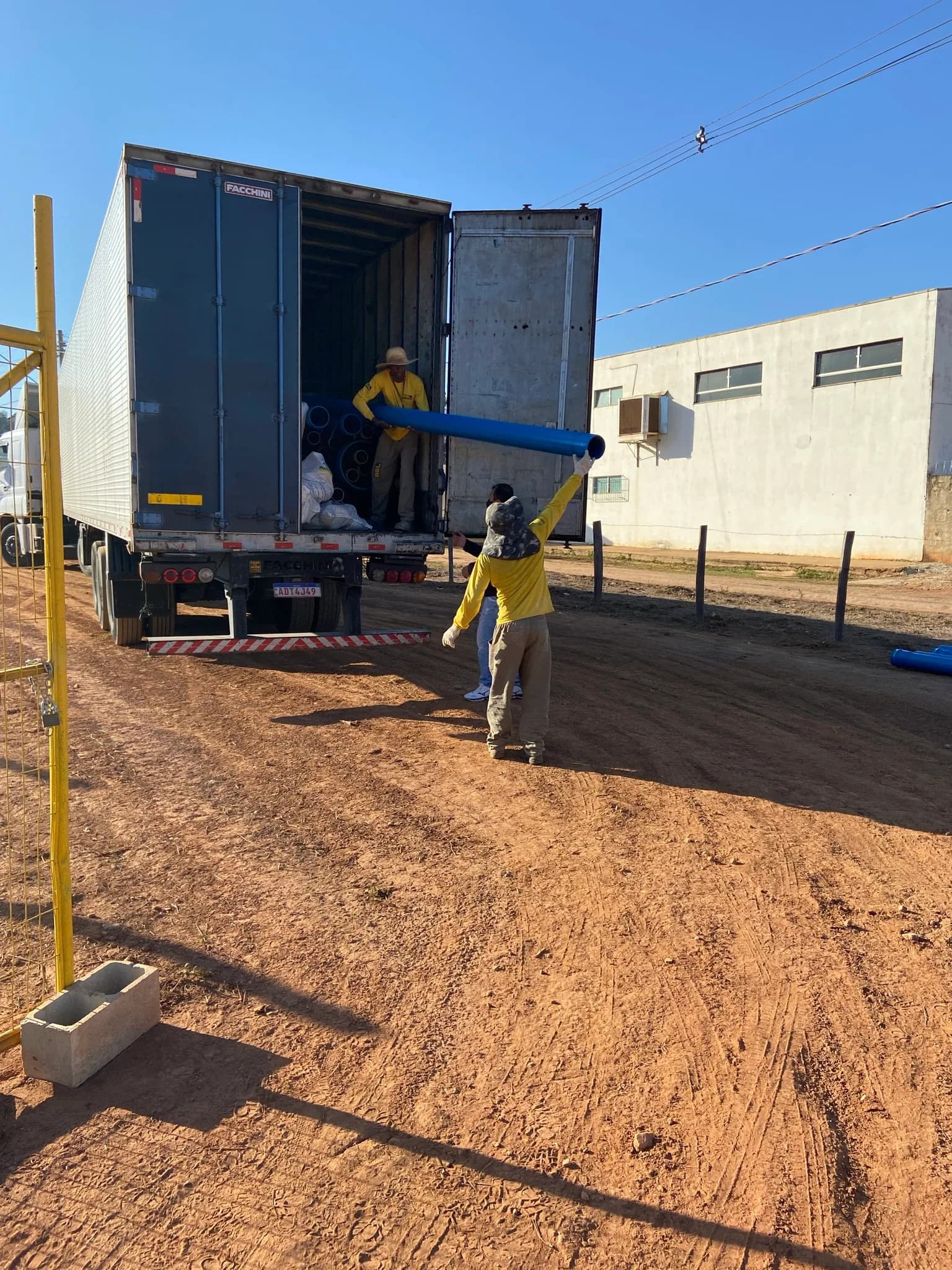 Trabalhadores descarregando tubos azuis de PVC