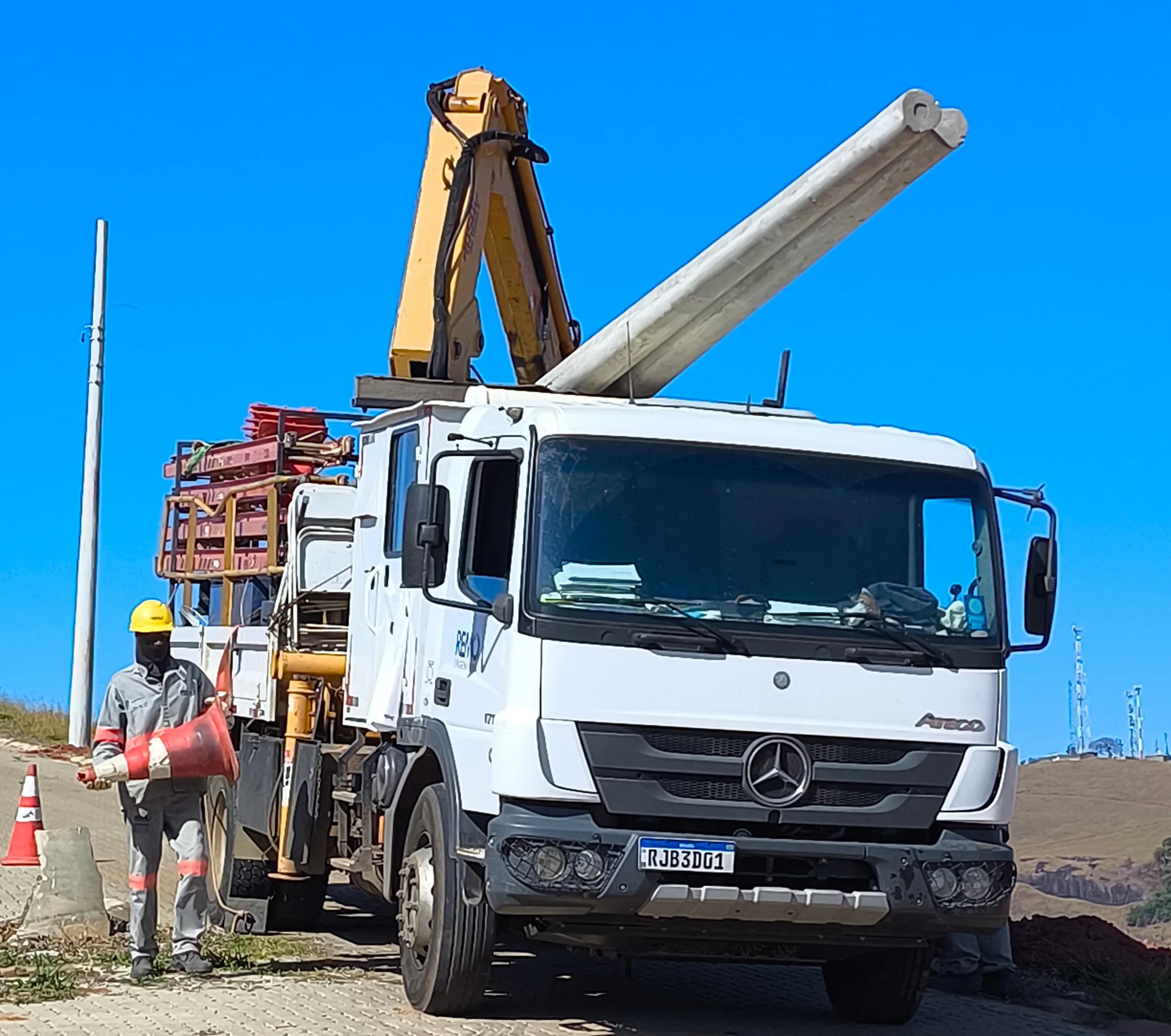 Caminhão com guindaste e postes de concreto no canteiro
